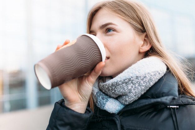 The girl walks down the street with a paper Cup of coffee, close-up, good weather, woman in jacket, isolated