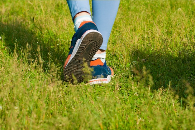 A girl walks on the grass view of her legs from behind