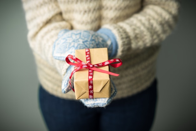 A girl in a warm knitted sweater and mittens is holding a Christmas present.