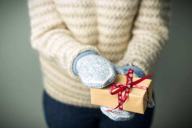 A girl in a warm knitted sweater and mittens is holding a Christmas present.