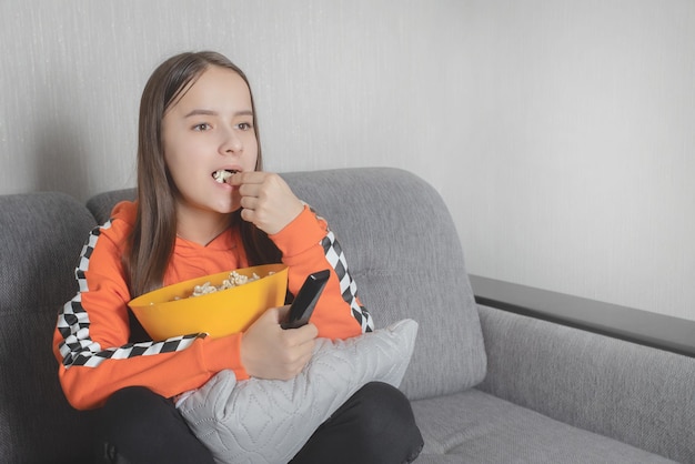 Girl watching a movie sitting with the remote control on the couch eating popcorn