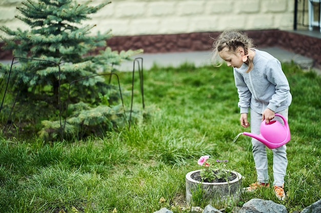 Girl watering a flowerbed from a watering can in the garden