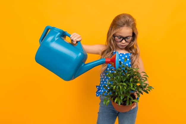 Photo girl watering a potted houseplant on a yellow with copy space