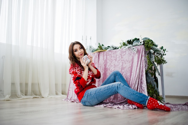 Girl wear on winter sweater sitting against table at room with chrismas decorations.