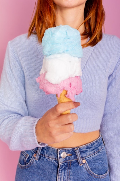 Girl wearing blue sweater and jeans and holding a cotton candy ice cream. Light pink background.