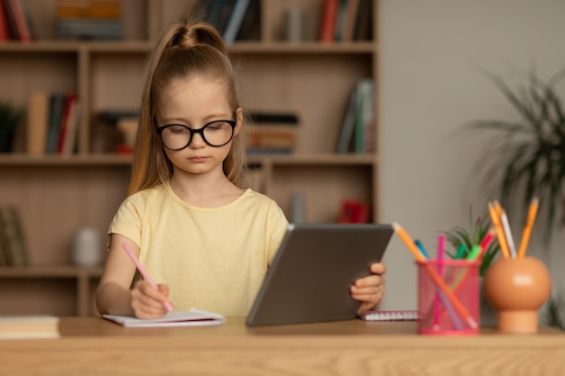 Girl Wearing Eyewear Using Tablet Learning Online Taking Notes Indoors