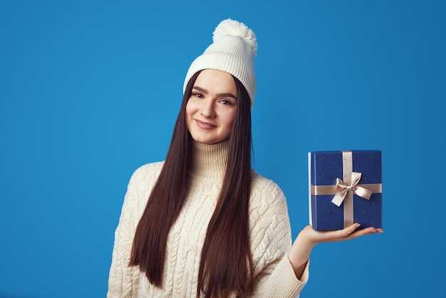 Girl wearing white oversize sweater and hat holding present box for