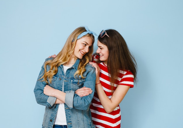 A girl whispers something in her girlfriend's ear by looking at her cell phone