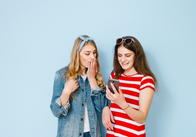 A girl whispers something in her girlfriend's ear by looking at her cell phone