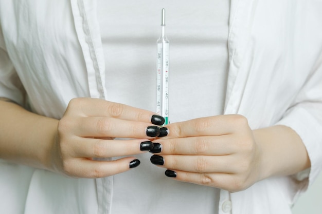 A girl in a white coat holds a thermometer to measure body temperature a medical worker a nurse H