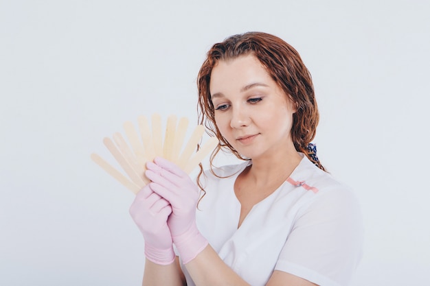 A girl in a white coat with wooden sticks in her hands. the doctor is preparing for waxing. Medicine concept, medical instruments, health care , beauty industry, hair removal, natural material