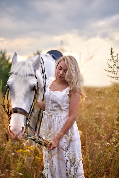 Girl in white dress holding a horse in the field