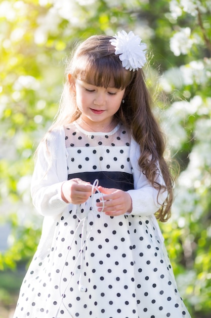 A girl in a white dress is holding an audio headphone.