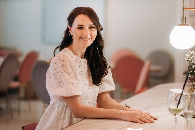 A girl in a white dress is sitting at the bar in a cafe and drinking a cocktail