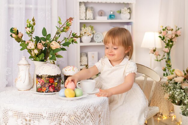 A girl in a white dress is sitting at a table and watching Easter holiday