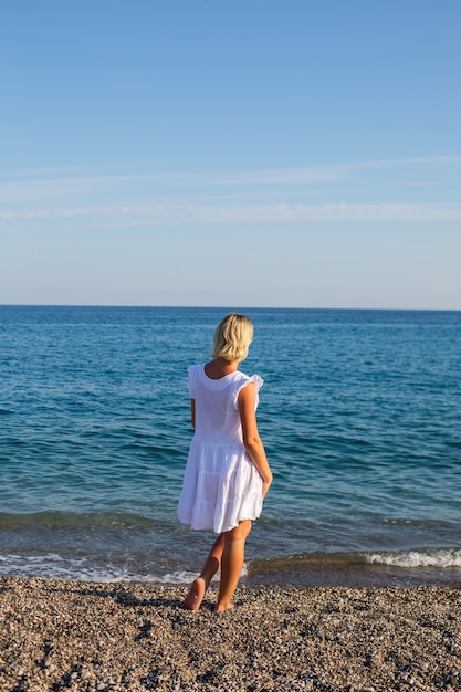 A girl on white dress walking by the sea