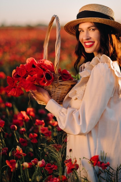 A girl in a white dress and with a basket of poppies walks through a poppy field