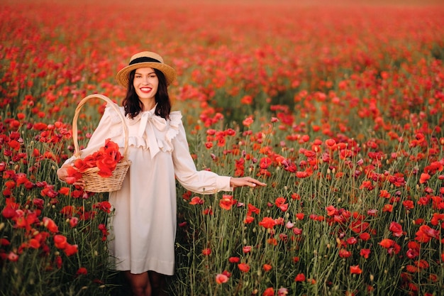 A girl in a white dress and with a basket of poppies walks through a poppy field