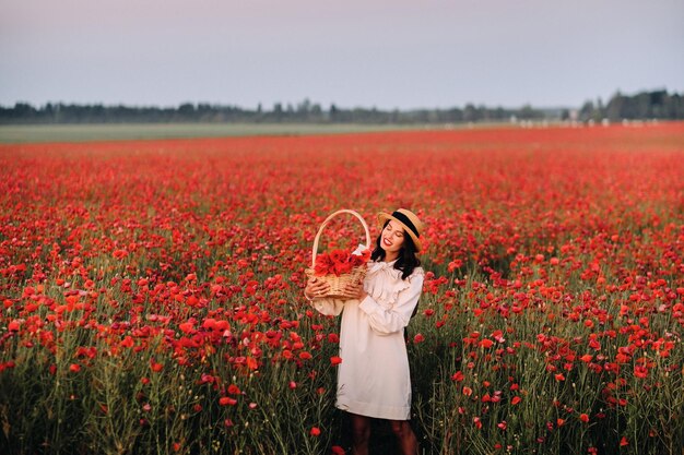 A girl in a white dress and with a basket of poppies walks through a poppy field