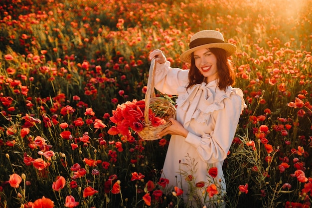 A girl in a white dress and with a basket of poppies walks through a poppy field