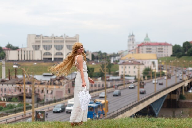 A girl in a white dress with white sun umbrella posing on city background.