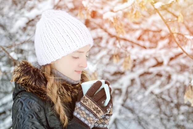 Girl in a white hat in winter with cup of tea side view close up