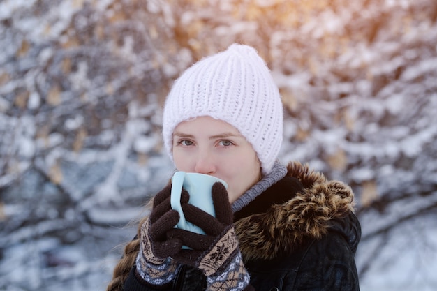 Girl in a white hat with a cup of tea among the snow-covered tree branches