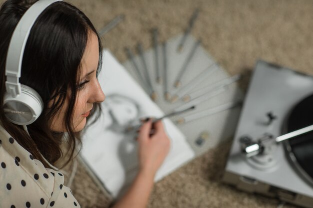 girl in white headphones draws while listening to an old vinyl record player