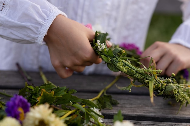 A girl in a white loose shirt makes a wreath of colorful wildflowers