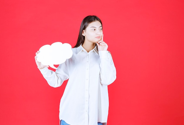 Girl in white shirt holding a cloud shape info board and looks confused and thoughtful