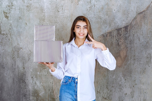 Girl in white shirt holding silver gift boxes and sending peace.