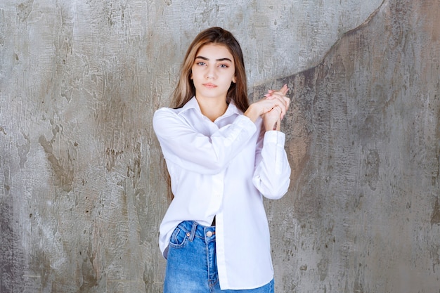 Girl in white shirt standing on a concrete wall and looks confused and thoughtful.