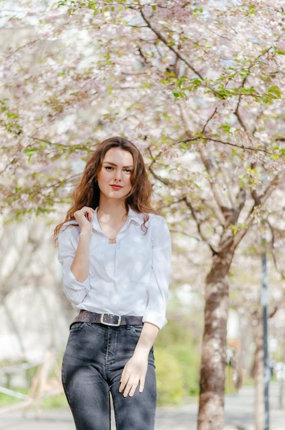 girl in a white shirt stands near the blossoming sakura