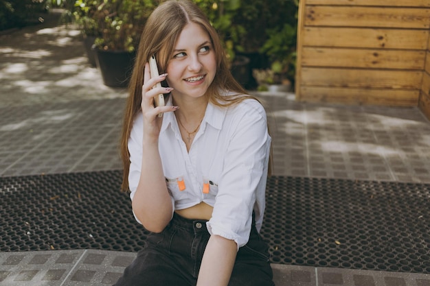 A girl in a white shirt in town talking on the phone