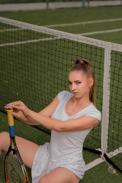 A girl in a white sports dress stands on a tennis court and holds a racket portrait of a girl on the tennis court