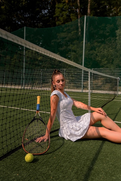 A girl in a white sports dress stands on a tennis court and holds a racket portrait of a girl on the tennis court