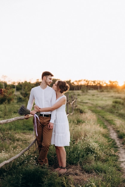 Girl in a white sundress and a guy in a white shirt on a walk at sunset with a bouquet in a village outside the city