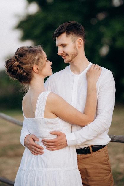 Girl in a white sundress and a guy in a white shirt on a walk at sunset with a bouquet in a village outside the city