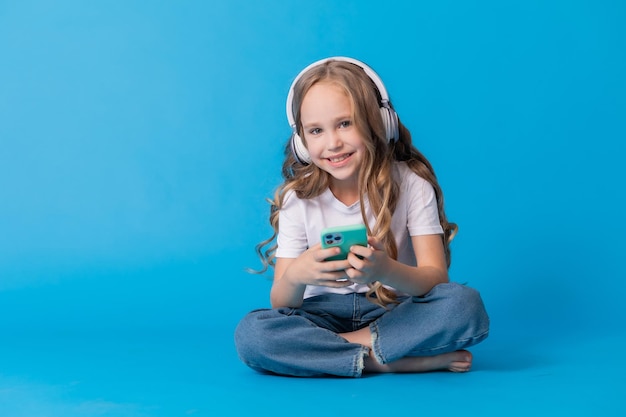 girl in a white T-shirt and jeans listens to music through headphones on a smartphone while sitting