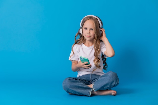 girl in a white T-shirt and jeans listens to music through headphones on a smartphone while sitting