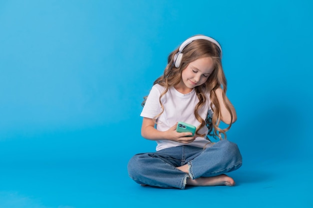 girl in a white T-shirt and jeans listens to music through headphones on a smartphone while sitting