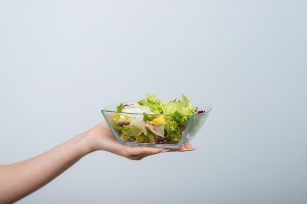 girl in a white tshirt holds a bowl of salad in her hands and eats