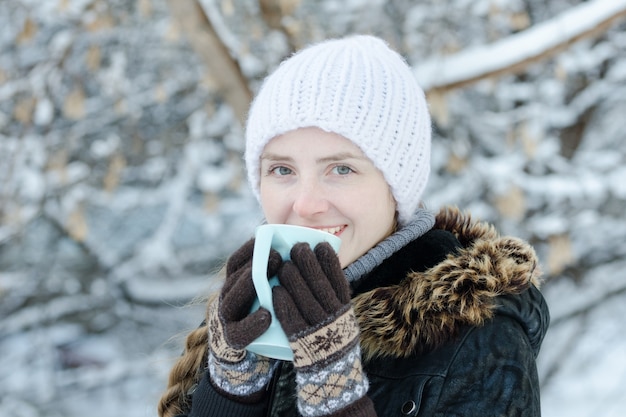 Girl in winter clothes drinking tea from a mug. Side view. close-up