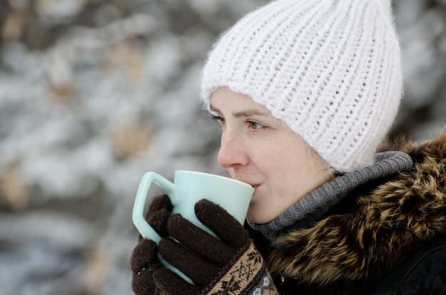 Girl in winter clothes drinking tea from a mug, side view, close-up