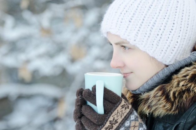 Girl in winter clothes drinking tea from a mug Side view closeup