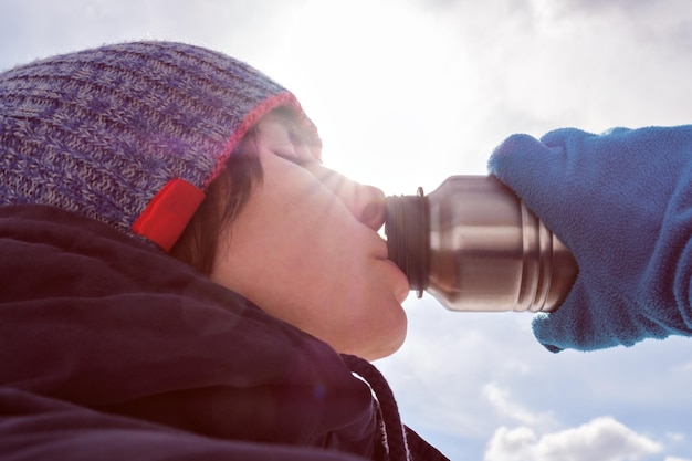 A girl in winter clothes eagerly drinks water from a bottle