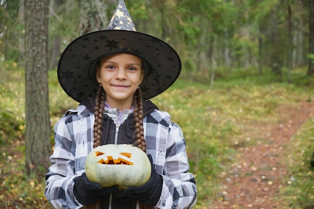 Girl in witch costume holding pumpkin lantern halloween concept girl in the forest playing with jack lantern