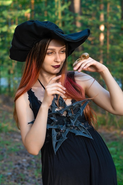 A girl in a witch costume with a pentagram around her neck is standing in the forestcostume idea for halloween and day of the dead