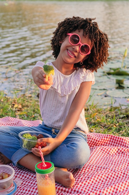 Girl with afro hair eating healthy salad from a glass container by the lake