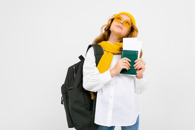 Girl with a backpack on her shoulders holds a passport with tickets for the rest on a white background with copy space.